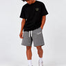 Bermuda de color gris oscuro con cordón blanco, logo en la pierna, modelo masculino con camiseta negra.