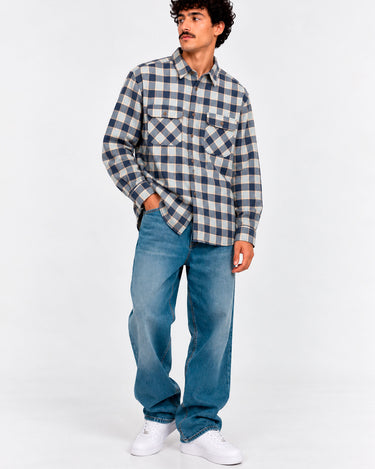 Camisa de franela de cuadros en tonos azul y gris, con dos bolsillos frontales, combinada con jeans claros.