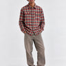 Camisa de franela de cuadros en tonos rojos y verdes, con dos bolsillos en el pecho, combinada con pantalones claros.