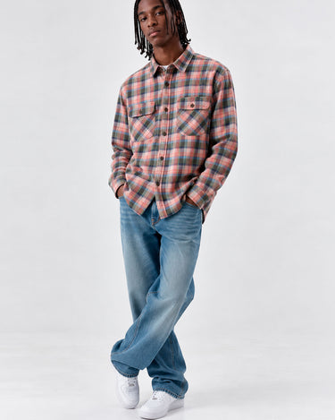 Camisa de franela de cuadros en tonos rosa y gris, con dos bolsillos frontales, combinada con jeans claros.