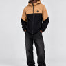 Cortavientos impermeable en negro y caramelo, con capucha y logo visible en el pecho, modelo de pie.