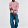 Jersey de hombre color rosa, tejido de punto, con mangas largas y cuello redondo, combinado con jeans azules.