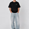 Pantalón vaquero claro de corte amplio, combinado con camiseta negra, modelo masculino posando en fondo gris.