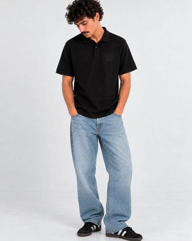Polo negro de hombre con logo en el pecho, combinado con jeans claros y zapatillas negras.