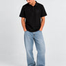 Polo negro de hombre con logo en el pecho, combinado con jeans claros y zapatillas negras.