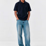 Polo navy de hombre con logo en el pecho, combinado con jeans claros y zapatillas blancas.