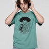 Camiseta verde con estampado en negro de personajes caricaturescos, modelo usando auriculares.