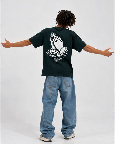 Camiseta negra con diseño de manos en la espalda, modelo de pie con jeans claros y brazos extendidos.