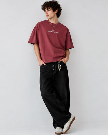 Camiseta boxy color púrpura con texto en el pecho, pantalones negros y zapatillas blancas, modelo de pie.