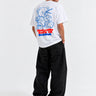 Camiseta blanca unisex con diseño azul de un oso y texto en rojo en la parte posterior, pantalones negros.