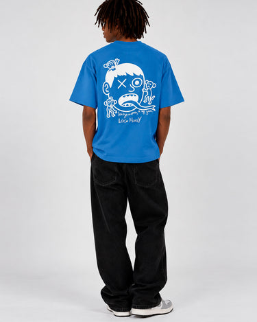 Camiseta azul con diseño gráfico en la espalda, hombre de pie con pantalones negros.