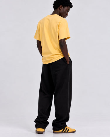 Camiseta amarilla suave con corte clásico, vista trasera, combinada con pantalones oscuros y zapatillas amarillas.