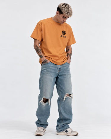 Camiseta mostaza con diseño en el pecho, combinada con jeans rotos y zapatillas blancas.