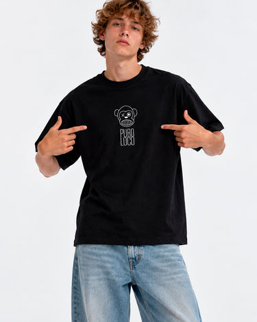 Camiseta negra unisex con diseño de oso y texto 'Puro Loco' en el pecho, modelo señalando el diseño.