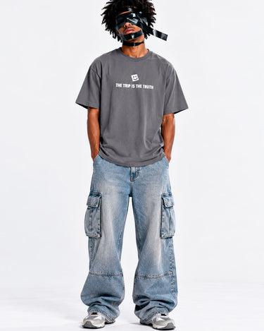 Camiseta gris oscuro con texto blanco "THE TRIP IS THE TRUTH" y pantalones anchos de mezclilla.