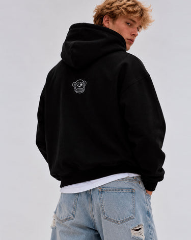 Sudadera oversize negra con capucha, diseño de logo de mono en la parte posterior, modelo masculino de cabello rizado.