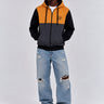 Sudadera con cremallera en mostaza, negro y gris oscuro, con capucha y logo en el pecho, modelo masculino con jeans rotos.