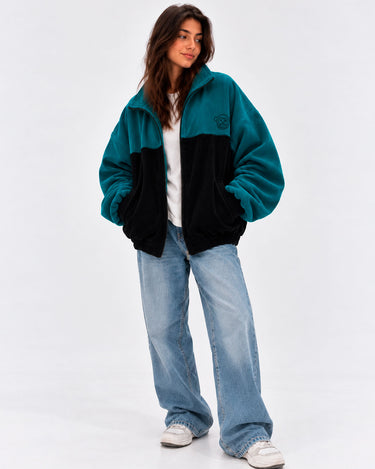 Chaqueta de pana oversize unisex en negro y azul océano, con logo en el pecho y pantalones de mezclilla claros.