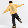 Sudadera unisex amarilla suave con diseño de un mono en la parte trasera, pantalones oscuros, persona de espaldas.
