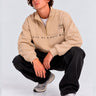 Sudadera oversize beige con logo bordado 'LOVE ME & HATE ME' en el pecho, modelo sentado, jeans negros.