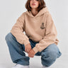 Sudadera unisex color arena con capucha, logo de Loco Monky en el pecho, combinada con jeans holgados.