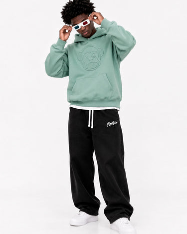 Pantalón oversize negro con detalles en blanco, combinado con sudadera verde claro y gafas de sol coloridas.