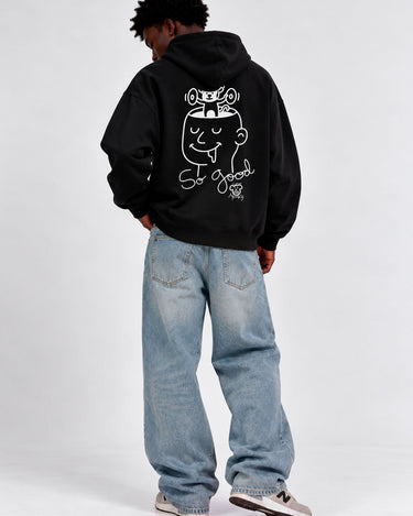 Sudadera negra con capucha, diseño gráfico en la espalda, jeans claros, modelo de pie de espaldas.