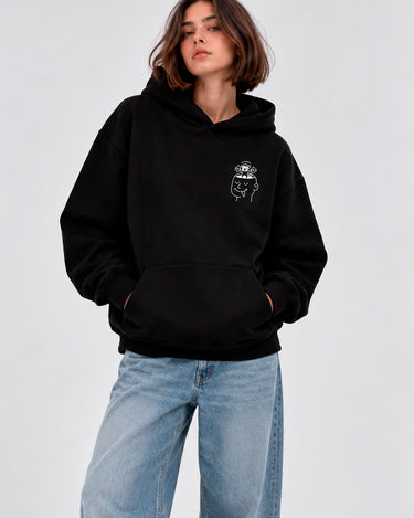 Sudadera unisex negra con diseño gráfico en el pecho y bolsillo frontal, modelo con jeans claros.