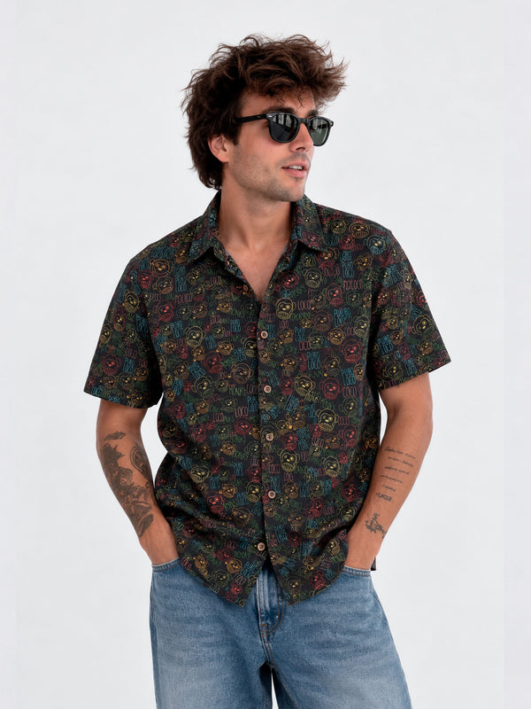 Camisa de hombre negra con estampado colorido, botones frontales y mangas cortas, combinada con gafas de sol.