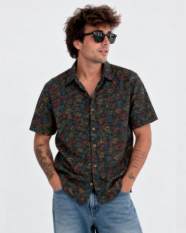 Camisa de hombre negra con estampado colorido, botones frontales y mangas cortas, combinada con gafas de sol.
