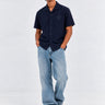 Camisa unisex de color navy con botones y logo en el pecho, combinada con jeans claros y zapatillas. Estilo casual.
