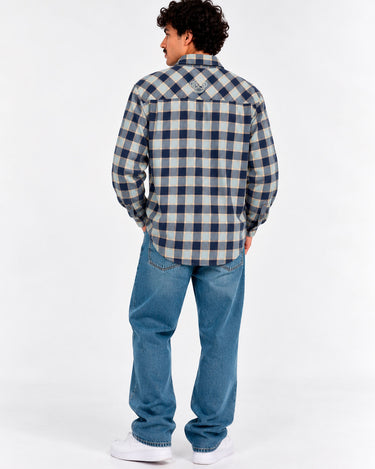 Camisa de franela de cuadros en tonos azul y gris, con logo en la parte posterior, combinada con jeans claros.