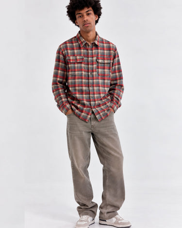 Camisa de franela de cuadros en tonos rojos y verdes, con dos bolsillos en el pecho, combinada con pantalones claros.