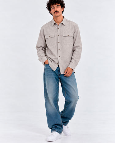Camisa de franela en color gris claro con dos bolsillos frontales, combinada con jeans azules y zapatillas blancas.