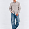Camisa de franela en color gris claro con dos bolsillos frontales, combinada con jeans azules y zapatillas blancas.