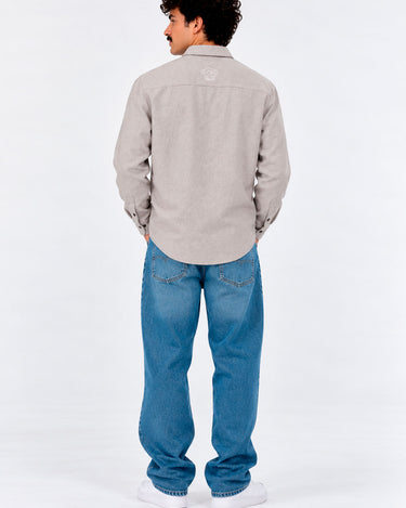 Camisa de franela gris claro con botones, vista trasera, combinada con jeans azules y zapatillas blancas.