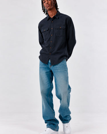 Camisa de franela navy con dos bolsillos frontales, combinada con jeans claros y zapatillas blancas.