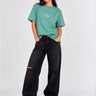 Camiseta verde con bordado en el pecho, combinada con pantalones negros rotos y calzado claro.