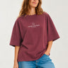 Camiseta boxy unisex color púrpura con texto blanco "THE TRIP IS THE TRUTH" en el pecho, modelo femenino sonriente