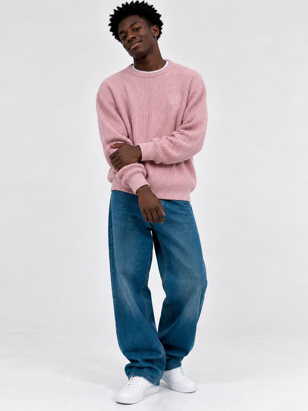 Jersey de hombre color rosa, tejido de punto, con mangas largas y cuello redondo, combinado con jeans azules.