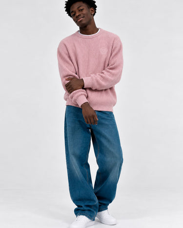 Jersey de hombre color rosa, tejido de punto, con mangas largas y cuello redondo, combinado con jeans azules.