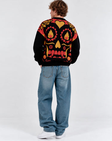 Jersey unisex negro con diseño colorido de calavera y corazones, visto desde atrás, combinado con jeans claros.