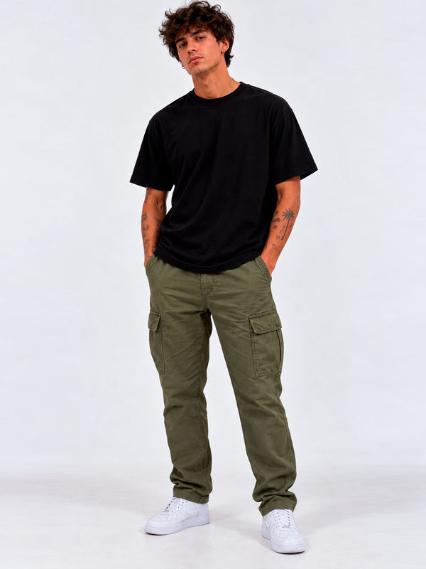Pantalón cargo verde con bolsillos laterales, combinado con camiseta negra y zapatillas blancas.