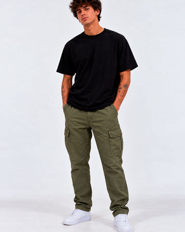 Pantalón cargo verde con bolsillos laterales, combinado con camiseta negra y zapatillas blancas.