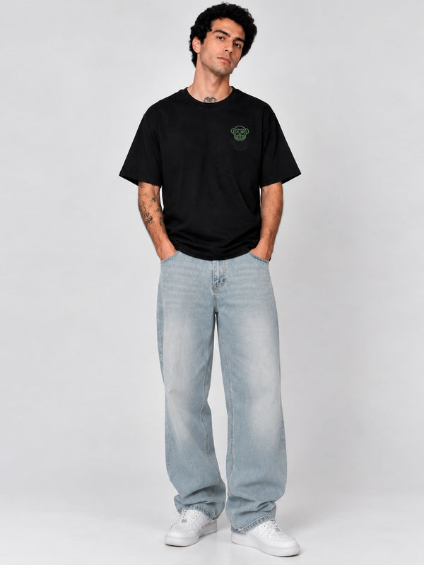 Pantalón vaquero claro de corte amplio, combinado con camiseta negra, modelo masculino posando en fondo gris.