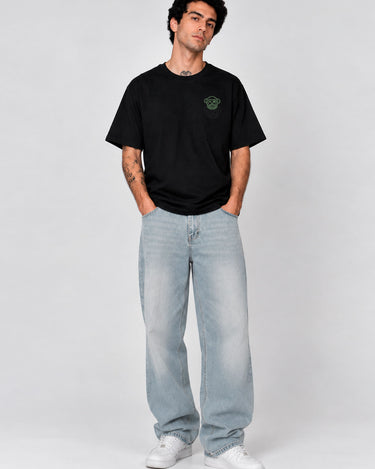 Pantalón vaquero claro de corte amplio, combinado con camiseta negra, modelo masculino posando en fondo gris.