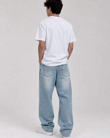 Pantalón vaquero azul claro con detalles de desgaste, modelo de hombre visto desde atrás, camiseta blanca.