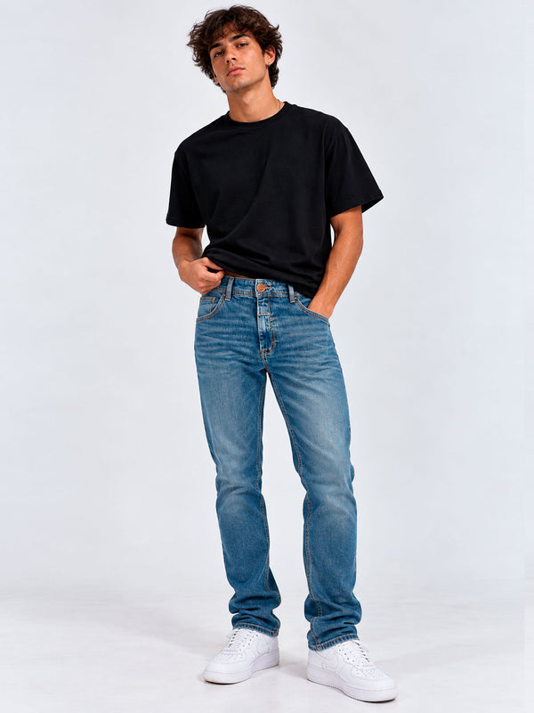 Pantalón vaquero azul claro para hombre, con camiseta negra y zapatillas blancas, fondo blanco