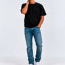 Pantalón vaquero azul claro en un hombre con camiseta negra y zapatillas blancas, fondo gris claro.
