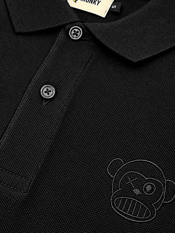 Polo negro con cuello, botones y logo de un mono en el lado izquierdo del pecho.